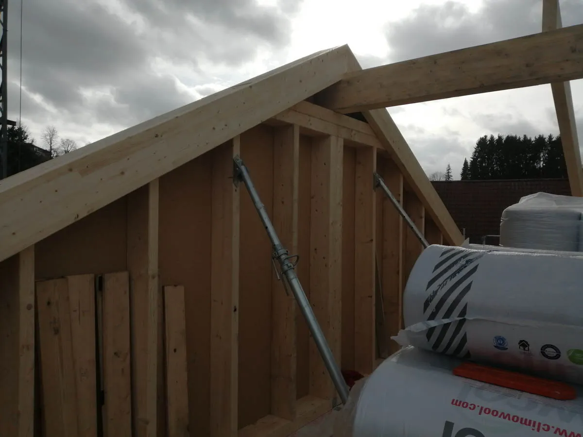 Holzständerwand eines Anbaus mit montierten Sparren und abgestützter Dachkonstruktion während der Bauphase