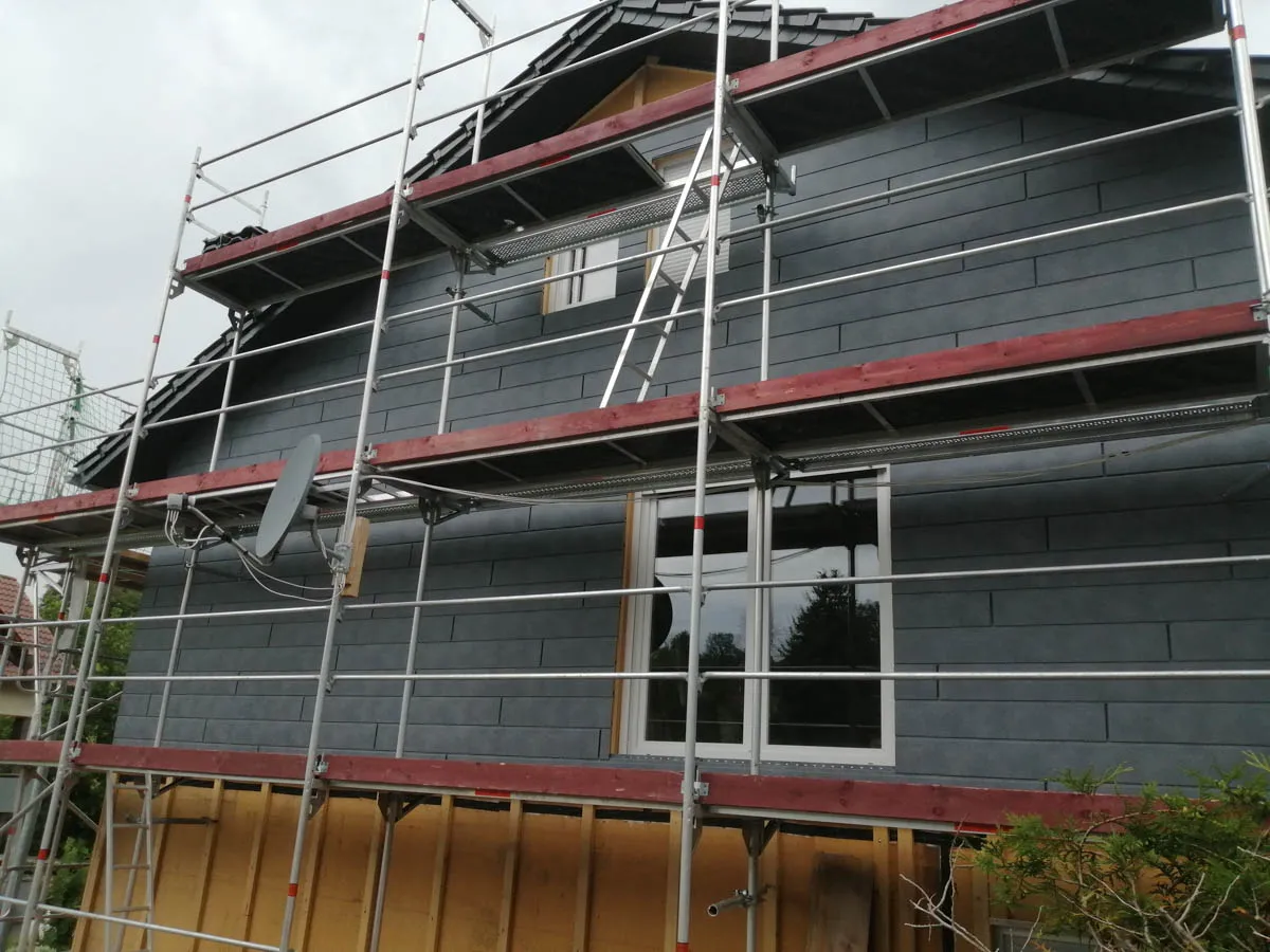 Fertig montierte Fassadenbekleidung aus Schieferoptik auf einem Wohnhaus mit eingerüsteter Außenwand