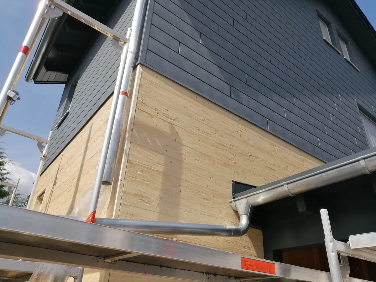 Außenecke eines Wohnhauses mit moderner Fassadenverkleidung und sichtbarer Holzfassade im unteren Bereich