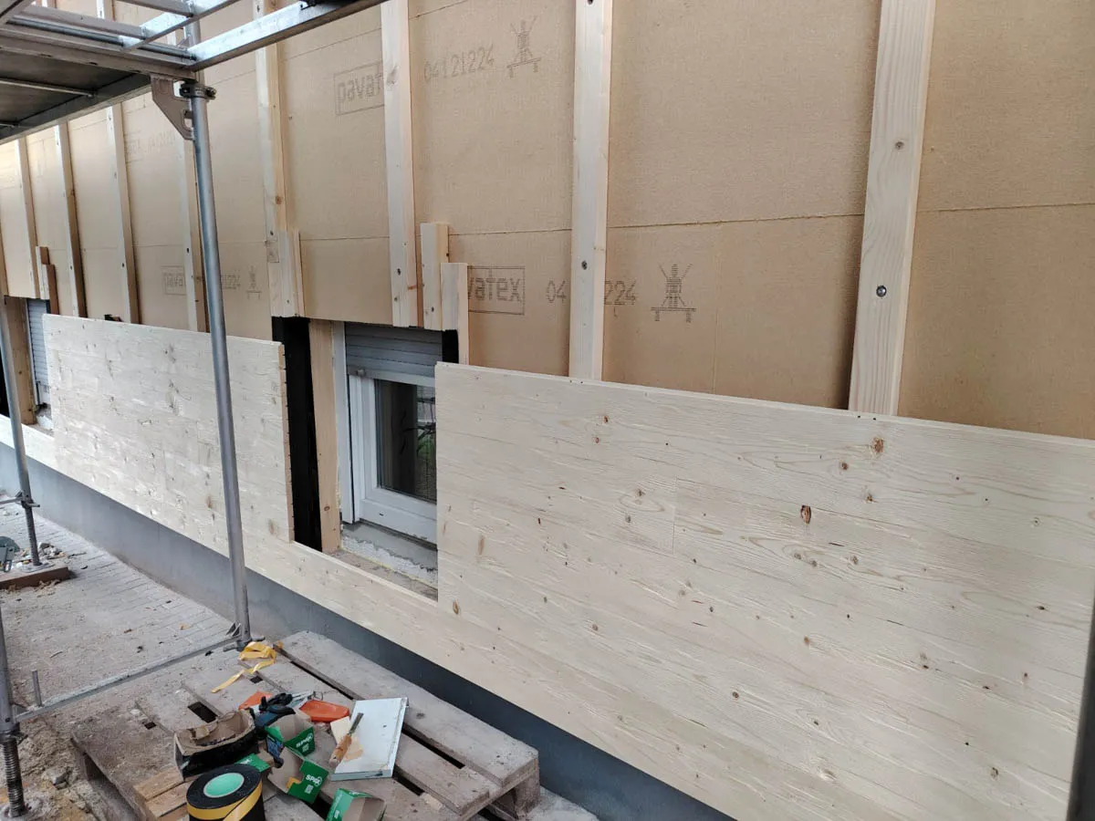 Holzfassade im Aufbau mit montierten Fassadenplatten und eingerüsteter Außenwand